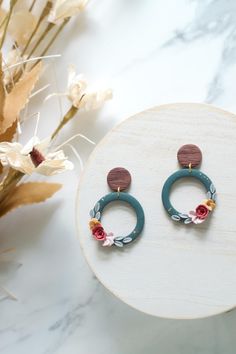 a pair of earrings sitting on top of a white table next to flowers and leaves