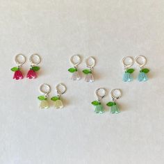 six charms with flowers and leaves are on a white surface, one has a green leaf