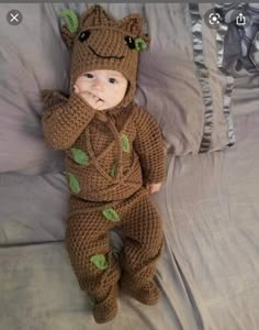 a baby in a crocheted frog outfit laying on a bed