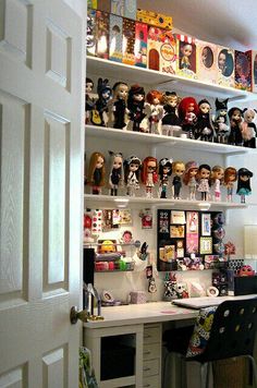 a white desk topped with lots of toy figurines next to a wall filled with pictures