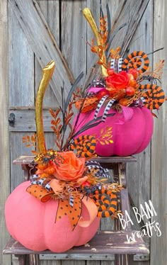 two pink pumpkins decorated with orange and black decorations on a wooden bench in front of a fence