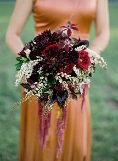 a woman in an orange dress holding a bouquet of red and white flowers on her wedding day