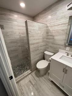 a white toilet sitting under a bathroom mirror next to a walk in shower and sink