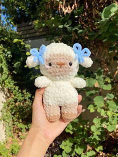 a hand holding a small crocheted stuffed animal in front of some bushes and trees