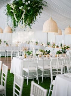 tables and chairs are set up in a tent for an outdoor wedding reception with greenery hanging from the ceiling