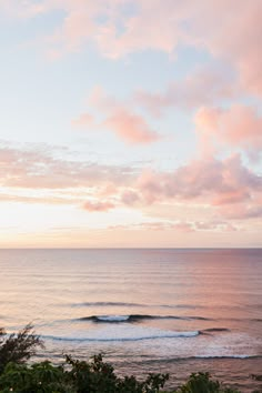 the sun is setting over the ocean with waves coming in from the water and trees on the shore