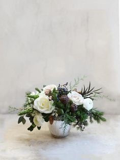 a vase filled with white flowers and greenery on a counter top next to a wall