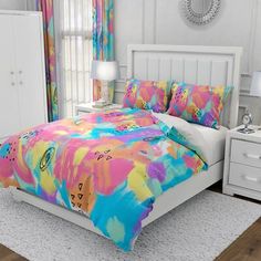 a bed with colorful comforter and pillows in a room next to a dresser, mirror and window