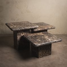 two marble tables sitting on top of each other in front of a beige wall and floor