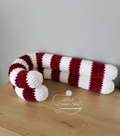 a red and white knitted candy cane sitting on top of a wooden table