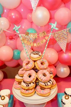 a table topped with donuts covered in frosting and sprinkles next to balloons