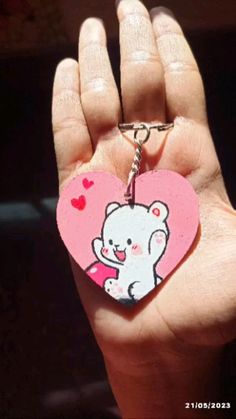 a hand holding a pink heart shaped keychain with a white bear on it