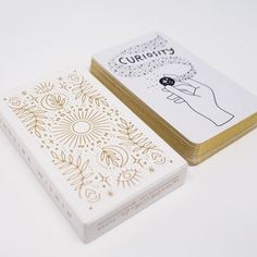 two playing cards sitting next to each other on a white surface with gold foiling