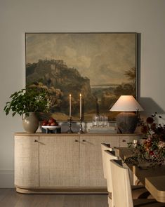 a dining room table with two vases on it and candles in front of the painting