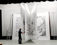 a man is standing in front of three large white panels with drawings on them and writing on the wall