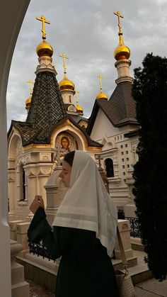 a woman standing in front of a church with gold crosses on it's roof