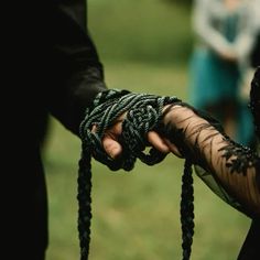 two people holding hands with black and green laces on their fingers, in front of some other people