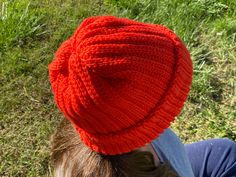 a person wearing a red knitted hat on top of their head in the grass