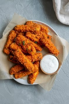 fried chicken sticks on a plate with ranch dressing and dipping sauce in a bowl next to it