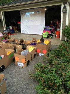 an image of people sitting in cardboard boxes on the ground with a projector screen behind them