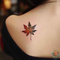 a leaf tattoo on the back of a woman's shoulder, with red and green leaves