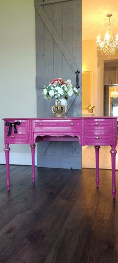 a pink table with flowers on it in front of a mirror and chandelier