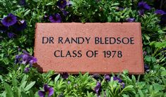 a brick sign that reads dr randy bledsone class of 788 surrounded by purple flowers