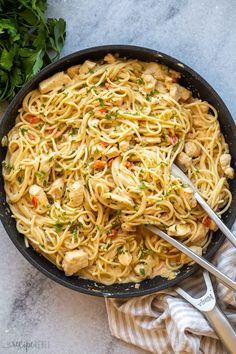 a skillet filled with pasta and chicken on top of a table next to parsley