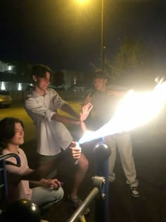 three people are sitting on the ground and one person is holding a lit sparkler