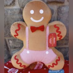 a stuffed ginger with a red bow tie and pink overalls sitting next to a brick wall