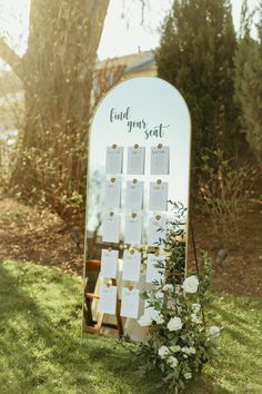 a mirror with seating cards on it and flowers in the grass next to it that says find your seat