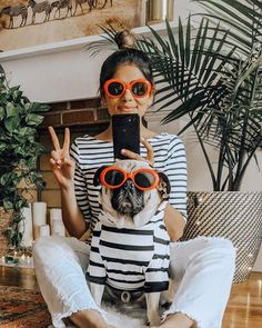 a woman sitting on the floor with her dog wearing sunglasses and holding up a cell phone