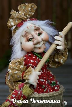 a close up of a doll holding a broom and wearing a red dress with white hair