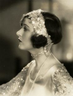 an old black and white photo of a woman in a dress with pearls on her head