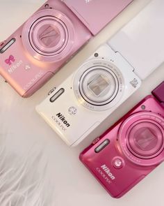 three pink and white digital cameras sitting next to each other on top of a bed