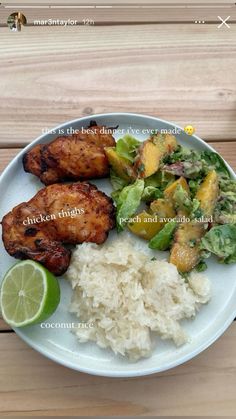 a white plate topped with chicken and rice next to a lime wedge on top of a wooden table