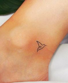 a small tattoo on the ankle of a woman's foot with a bird flying above it