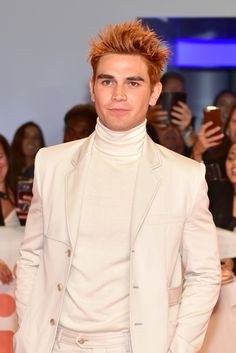 a young man with red hair wearing a white suit and posing for the camera at an event