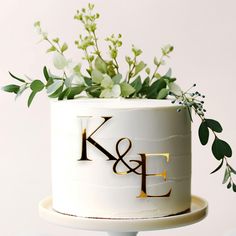 a wedding cake decorated with greenery and the initials k and f on it's side