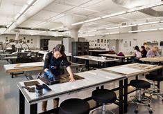 a woman is working in a large room with many tables and stools, while other people are sitting at desks