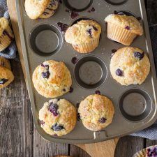 blueberry muffins in a muffin tin on top of a wooden table