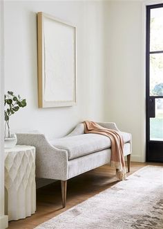 a white couch sitting in front of a window on top of a wooden floor next to a rug