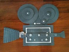 a paper cut out of an old movie projector on a wooden floor with the film reel attached to it