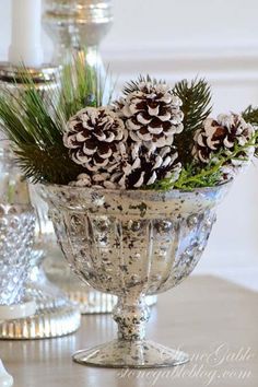 some pine cones are sitting in a glass bowl on a table with other christmas decorations