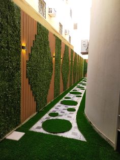 an artificial garden with grass growing on the walls and in between two buildings, there is a pathway that leads to another building