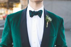 a man wearing a green jacket and bow tie with a boutonniere on his lapel