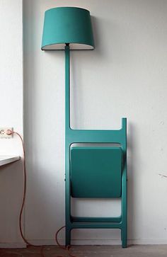 a green chair next to a white wall with a lamp on it