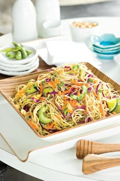 a plate with noodles, carrots and cucumbers on it next to other plates