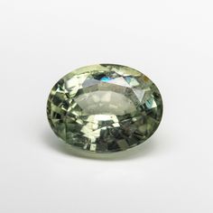 an oval shaped green diamond sitting on top of a white surface with one side facing the camera