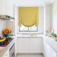 a kitchen with marble counter tops and white cabinets, along with a window covered in roman shades